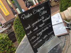 a menu sign sitting on the side of a sidewalk next to a table with an open book