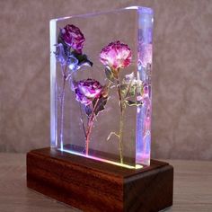 three purple flowers in a glass block on a wooden base with light up lighting behind them