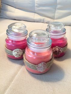 four jars filled with different colored candles sitting on a white couch next to a teddy bear