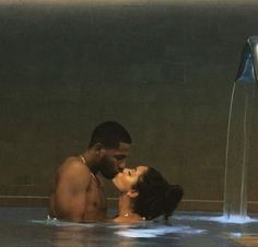 a man and woman are kissing in the middle of a pool with water shooting from it