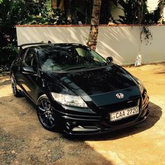 a black car parked in front of a white wall and palm tree on the other side