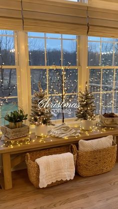 a table with baskets and christmas trees in front of a large window that has lights on the windowsill