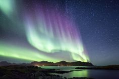 the northern lights shine brightly over water and mountains