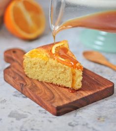 someone is pouring orange juice into a piece of cake on a cutting board next to an orange slice