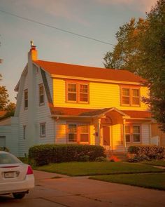 a white car parked in front of a yellow house with red roof and two windows