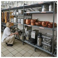 a woman kneeling down in front of shelves filled with pots and pans