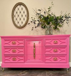 a pink dresser with gold handles and knobs on the doors is next to a potted plant