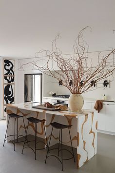 a modern kitchen with an island and bar stools in the center, surrounded by art work