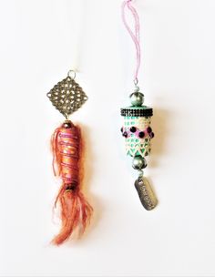 two ornaments hanging from strings on a white surface, one is pink and the other is silver