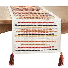 a table runner with tassels on it and a wooden bench in the background