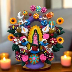 a statue of the virgin mary surrounded by flowers and birds on a table next to candles