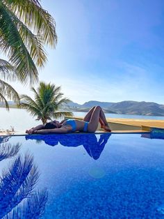 a woman laying on the edge of a swimming pool next to palm trees and water