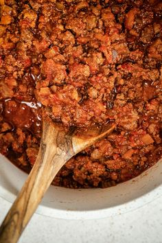 a wooden spoon in a pot filled with chili and meat sauce on top of a table