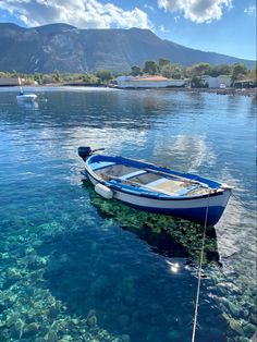 a small blue boat floating on top of a lake next to a shore covered in rocks