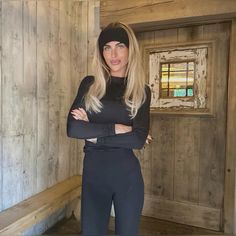 a woman standing in front of a wooden wall with her arms crossed and looking at the camera