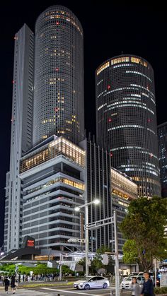 people are walking on the sidewalk in front of some tall buildings at night with bright lights