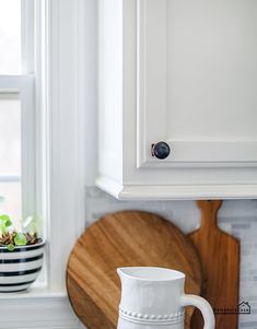 a white pitcher sitting on top of a counter next to a cutting board and window