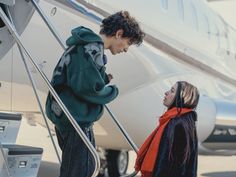 two people standing on the steps of an airplane and looking at each other's eyes