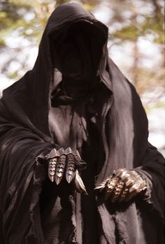 a man in a black hooded costume with horns and claws on his hands, standing outside