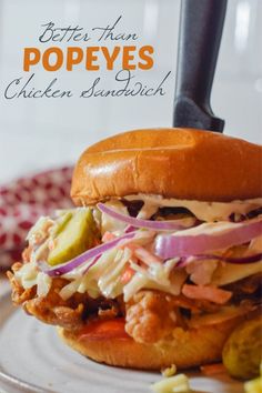 a chicken sandwich with coleslaw and pickles on a plate next to a knife