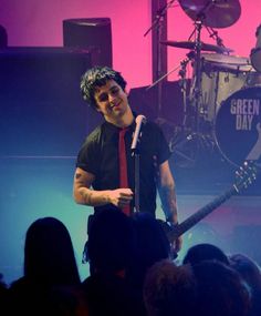 a man standing on top of a stage holding a guitar in front of a microphone