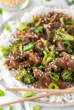 beef and broccoli stir - fry with rice on a white plate topped with chopsticks