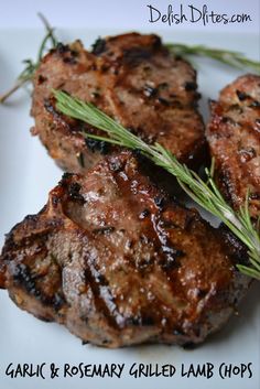 three pieces of meat on a white plate with rosemary sprigs and seasoning