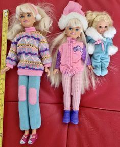 three dolls are laying next to each other on a red surface with a measuring tape