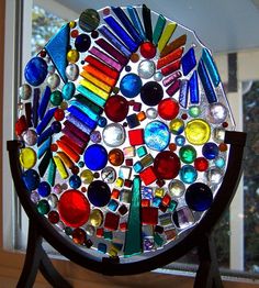 a multicolored glass plate sitting on top of a wooden stand next to a window