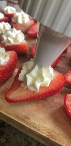 strawberries and whipped cream on a cutting board with a person using a knife to cut them