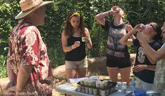 a group of young people standing around a table with drinks on it and one person holding a cell phone up to his ear