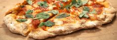 a close up of a pizza on a wooden table with basil and cheese toppings