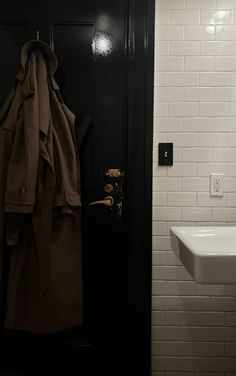 a coat hanging on the wall next to a white sink and black door in a bathroom