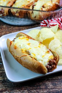 a chili cheese hot dog on a plate next to some potato chips and a casserole dish