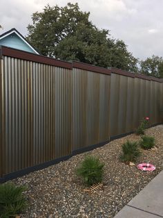 a long metal fence next to a gravel area with flowers and plants in the foreground