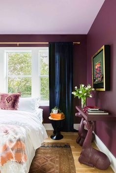 a bedroom with purple walls, white bedding and wooden flooring is decorated in an eclectic style