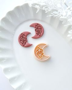 two decorated cookies sitting on top of a white plate next to each other, with the moon and rose cookie cutters