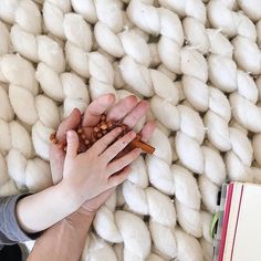 two hands reaching for something in front of a pile of white wool balls and a binder