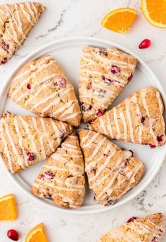 orange cranberry scones with icing on a white plate next to sliced oranges