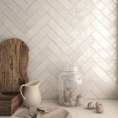 a kitchen counter with white herringbone tile on the wall and wooden cutting board next to it