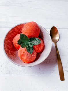 a white bowl filled with fruit on top of a wooden table next to a spoon