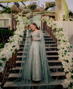 a woman in a long dress is standing on some stairs with flowers and greenery