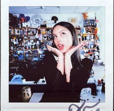 a woman making a funny face while sitting at a desk in front of a wall full of shelves