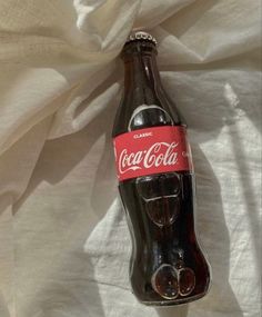 an empty coca cola bottle sitting on top of a white sheet