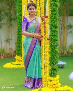 a woman in a blue and green sari standing next to flowers on the grass