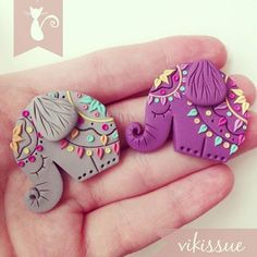 two small elephant brooches in the palm of someone's hand, one purple and one gray