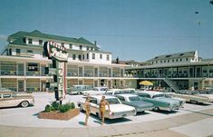 several cars parked in front of motels on a sunny day with people walking by