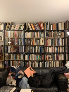 a man sitting on a couch reading a book in front of a bookshelf