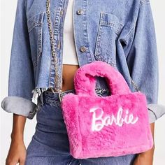 a woman holding a pink purse with the word barbie on it