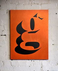 an orange and black painting hanging on a wall next to a white brick wall,